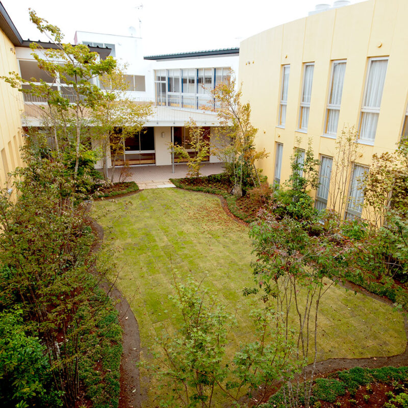 介護施設の中庭。芝生と低木植栽に囲まれた落ち着いた外構空間。